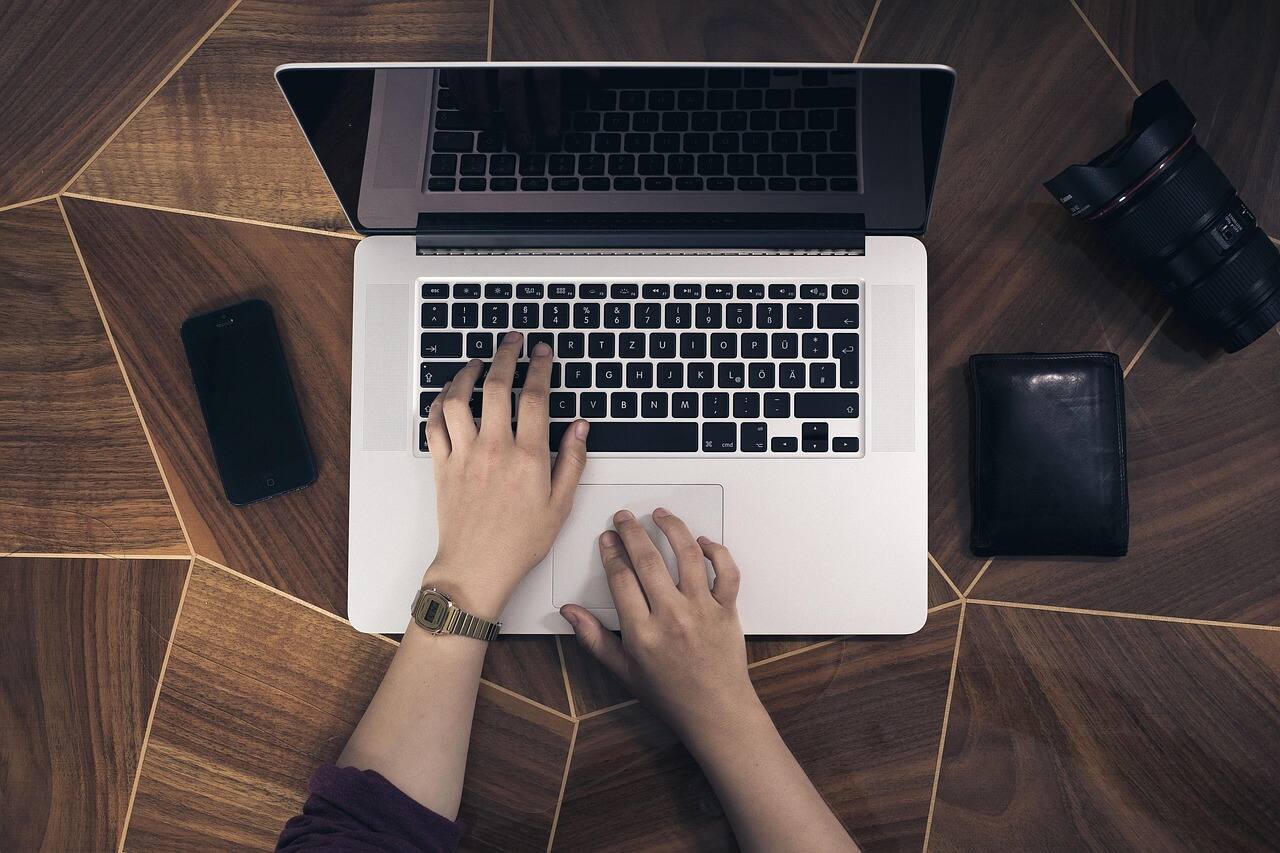 A person focused on typing on a laptop, with hands positioned over the keyboard and a soft light illuminating the scene.